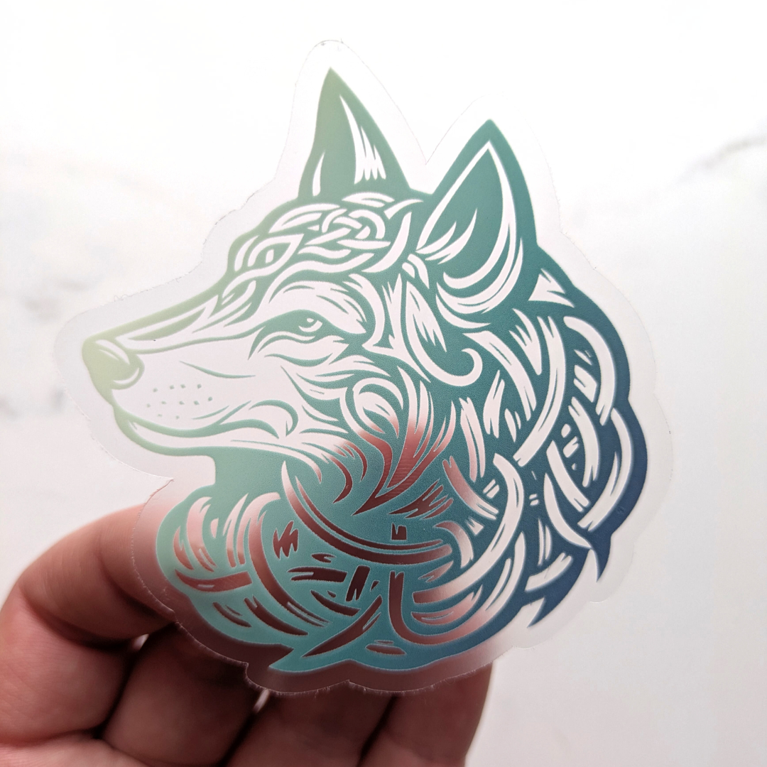 Translucent teal Celtic wolf sticker with intricate knotwork design on clear vinyl background held in hand