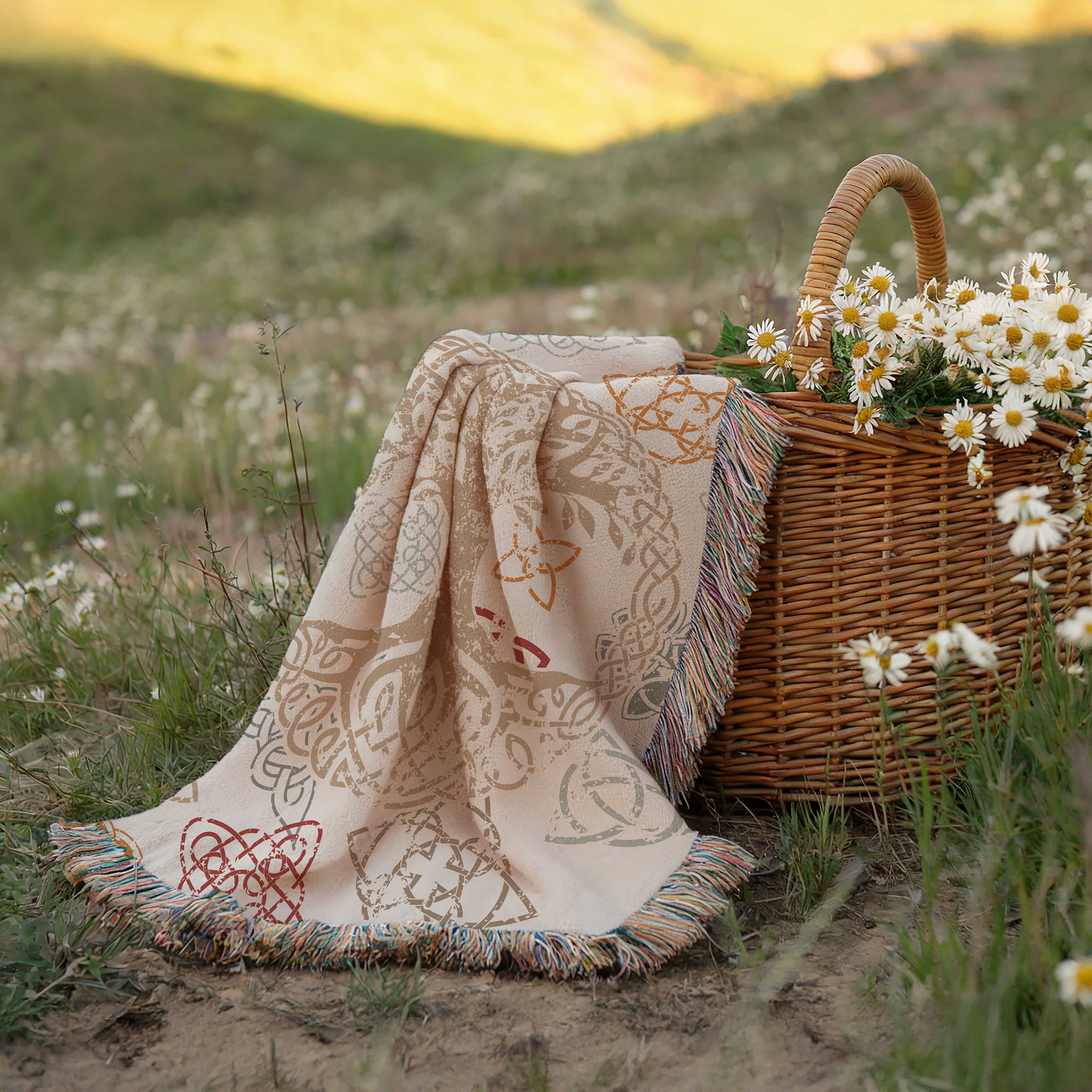 Decorative blanket on a wicker basket with flowers on a grassy field.