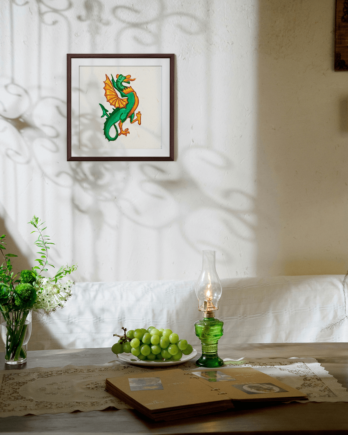 Framed artwork of a colorful dragon on a wall with a table and decorative items below.