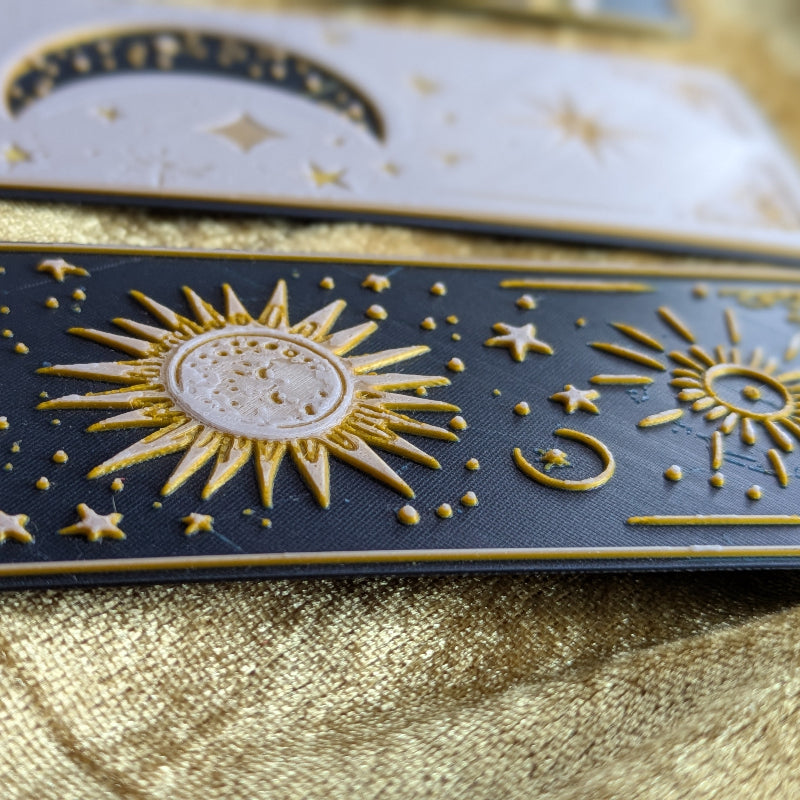 Close-up of three celestial bookmarks showing raised moon sun star and gold details