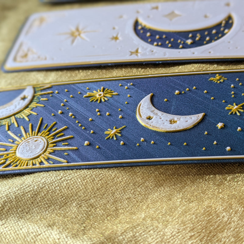 Close-up of three celestial bookmarks showing raised moon sun star and gold details