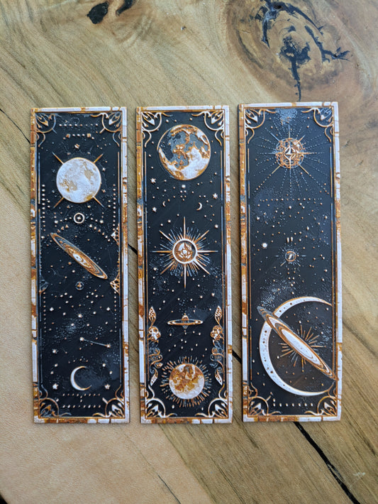 Set of 3 celestial-themed 3D-printed bookmarks featuring sunburst, Saturn & crescent moon, and lunar phases designs in gold and white.