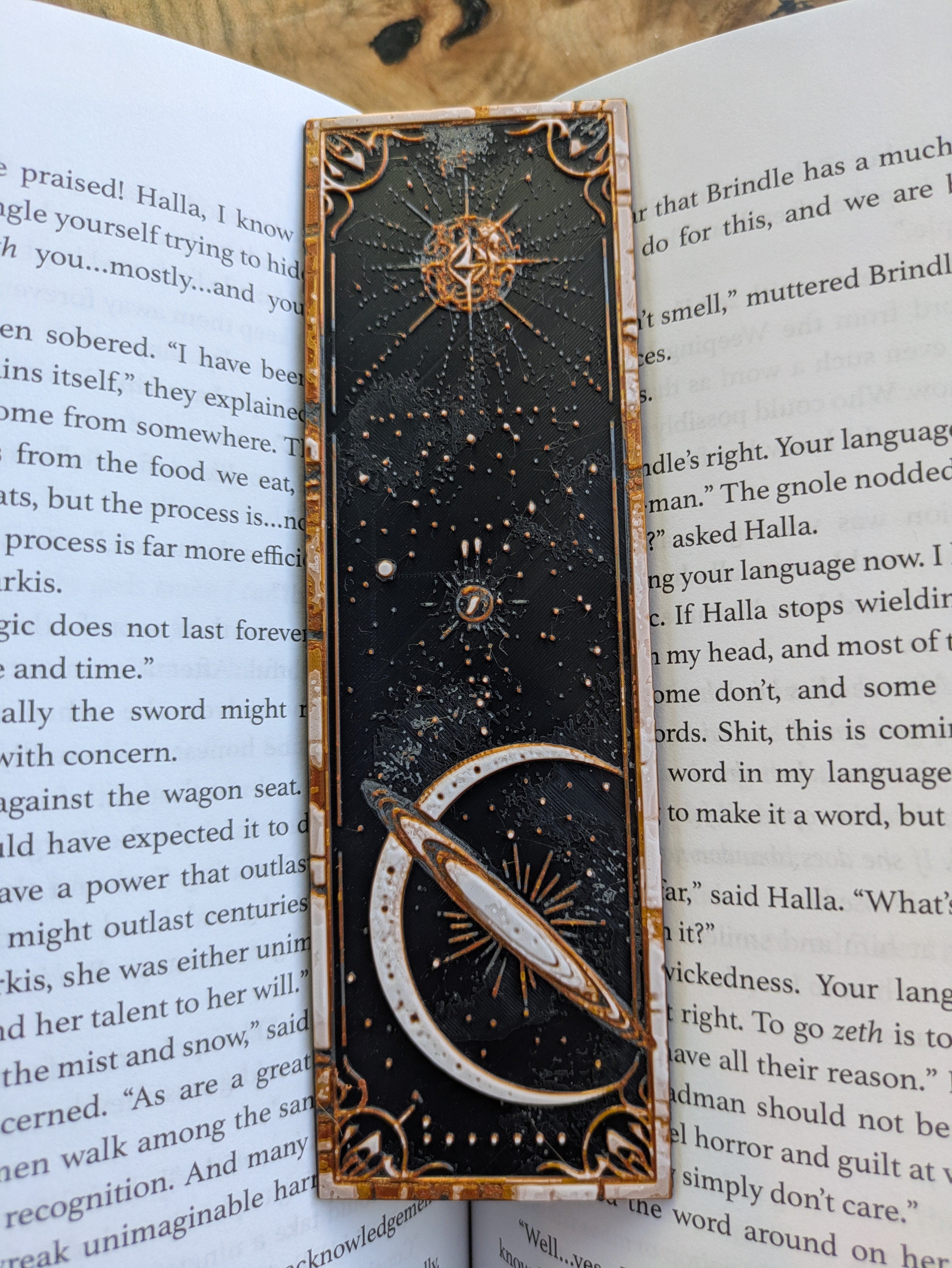 Celestial-themed 3D-printed bookmark featuring a gold and white sunburst design on a black background.