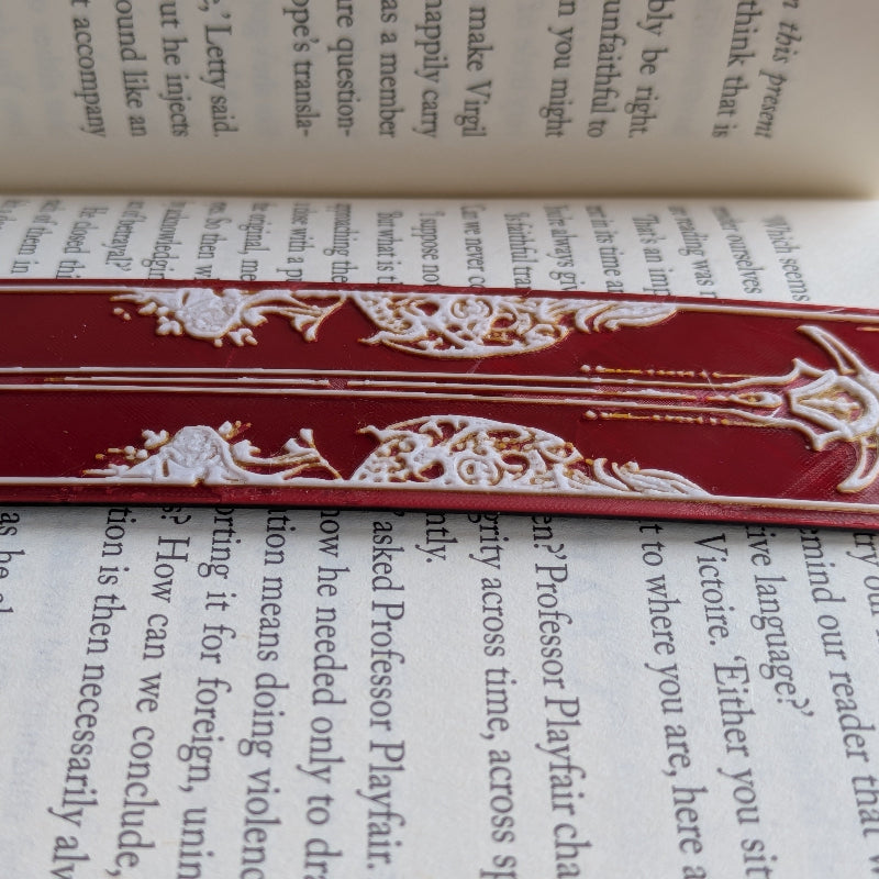 Close-up of crimson sword bookmark with gold accents and textured print surface