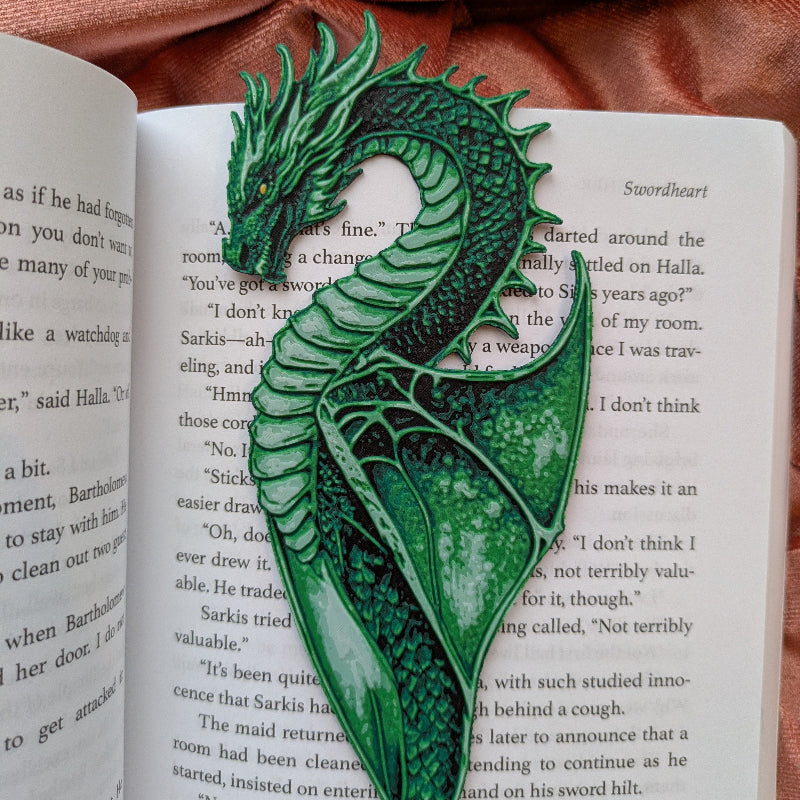 textured green dragon bookmark placed inside an open book with warm fabric background