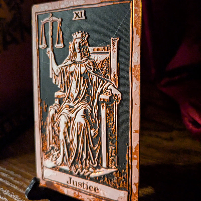 Angled close-up of the Justice tarot card bookmark Collector Edition, showing copper-toned relief detailing on the crowned figure and throne