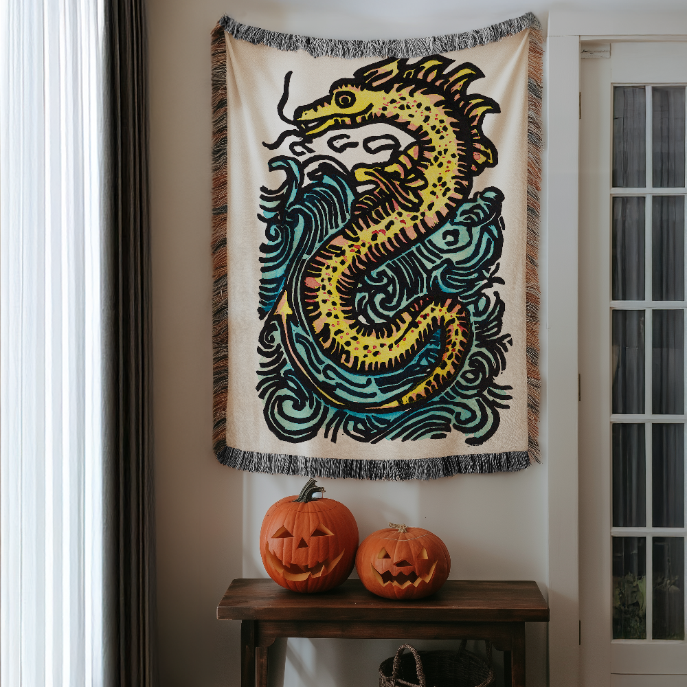 A cream-colored woven tapestry featuring a stylized yellow and teal sea serpent design, hanging on a door in a home interior above a wooden table with two carved pumpkins.