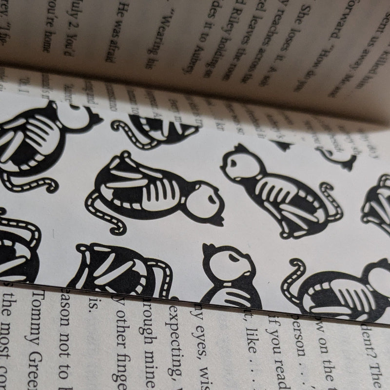 Close-up detail of black and white medieval cat skeleton pattern on paper bookmark showing linework texture