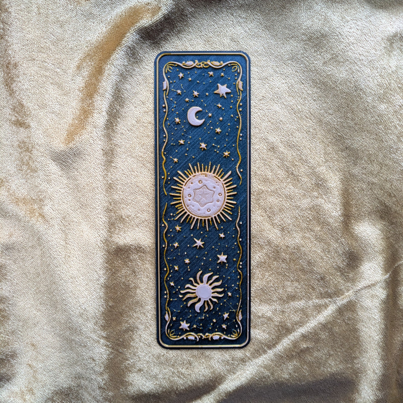 Gold embossed sun and moon face celestial bookmark on deep teal background