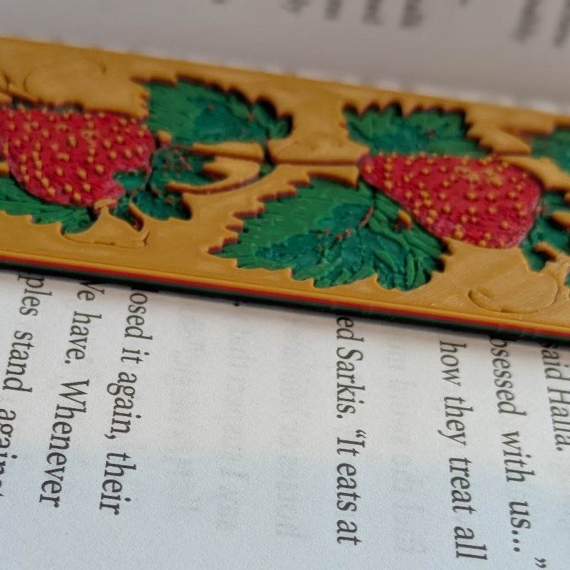 Close-up detail of textured strawberry bookmark with raised botanical artwork and medieval inspired design