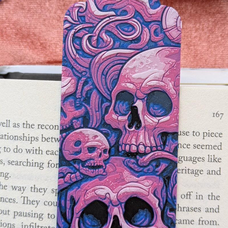 Close-up of pink and violet skull bookmark showing intricate gothic linework and fantasy-inspired details on textured artwork