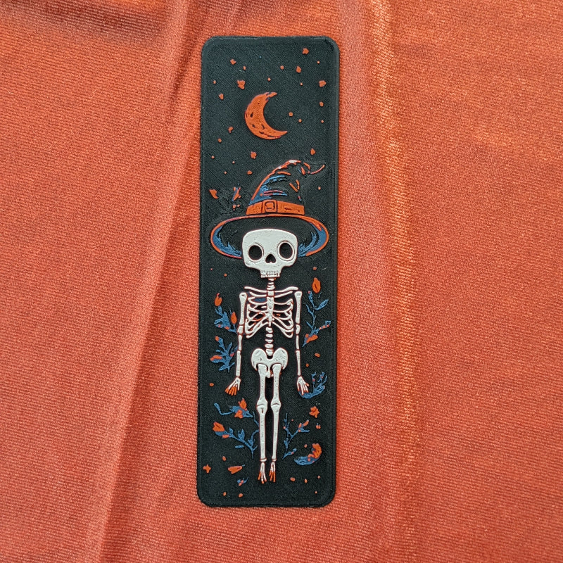 Textured 3D printed skeleton bookmark with witch hat and crescent moon on dark background
